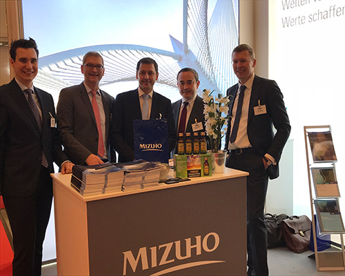 men standing behind a Mizuho booth at a conference
